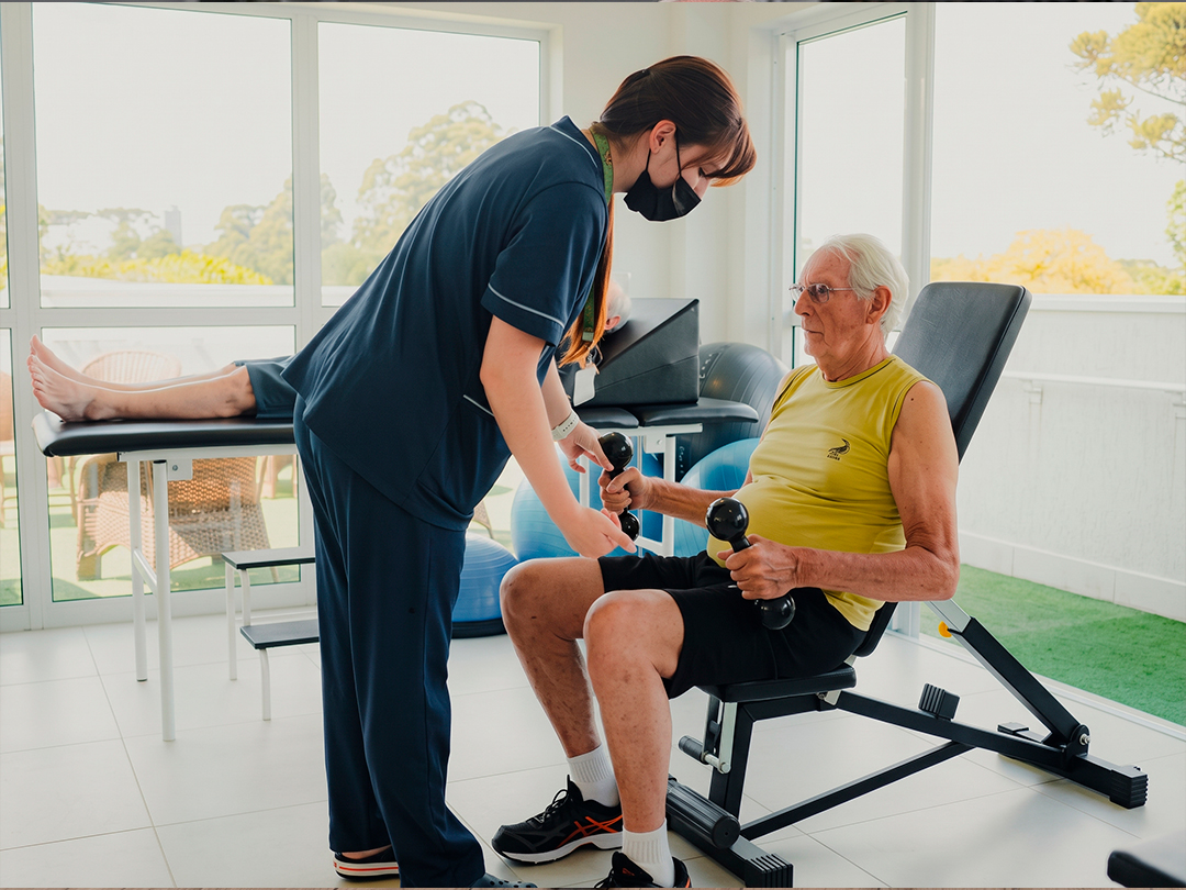 Pessoa idosa realizando exercício de força com acompanhamento profissional