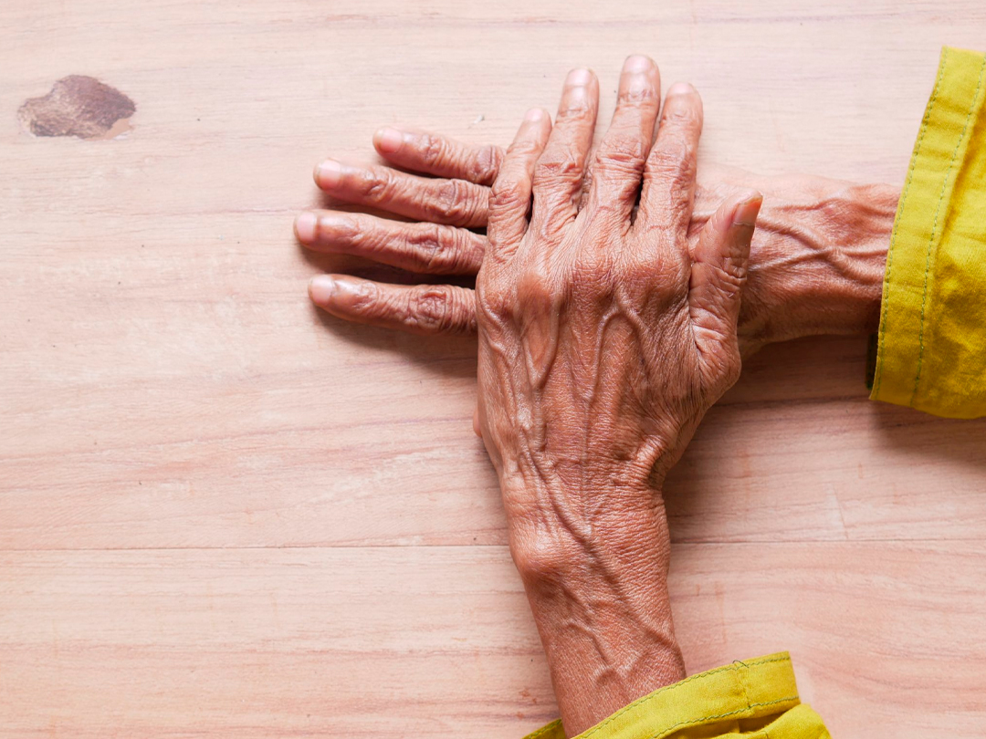 Mãos de uma pessoa idosa apoiadas sobre uma mesa